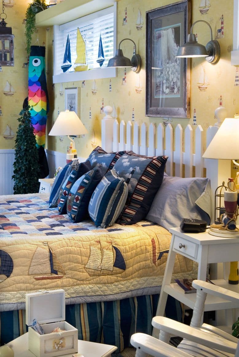 Bedroom at Baywood Shores Bed & Breakfast featuring a white picket fence headboard, nautical themed bedding, yellow wallpaper, and decorative elements.