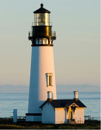 A tall white lighthouse stands next to a small house by the ocean.